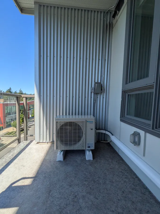 Heat pump outdoor unit on a condo balcony, wired to a wall-mounted disconnect switch