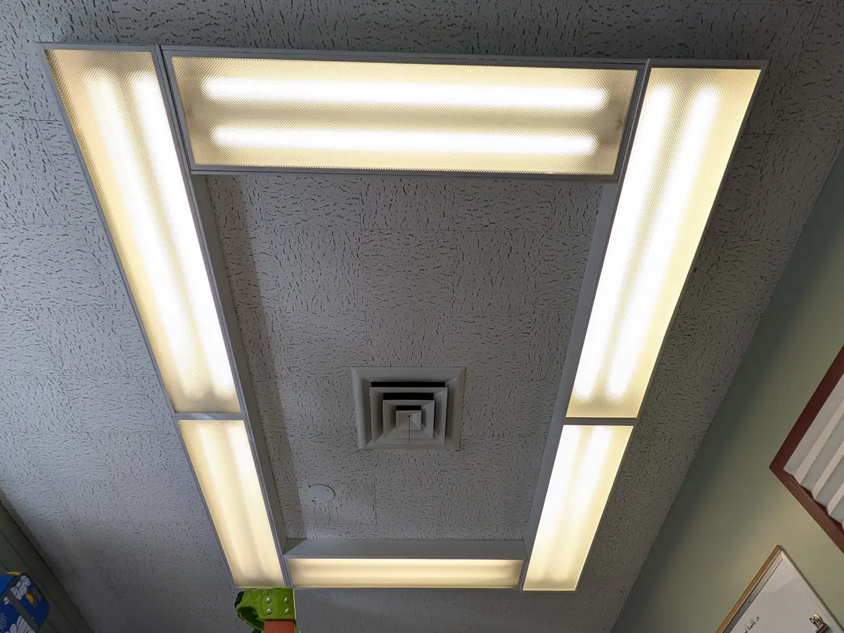 Rectangle of linear LED ceiling fixtures around an air vent
