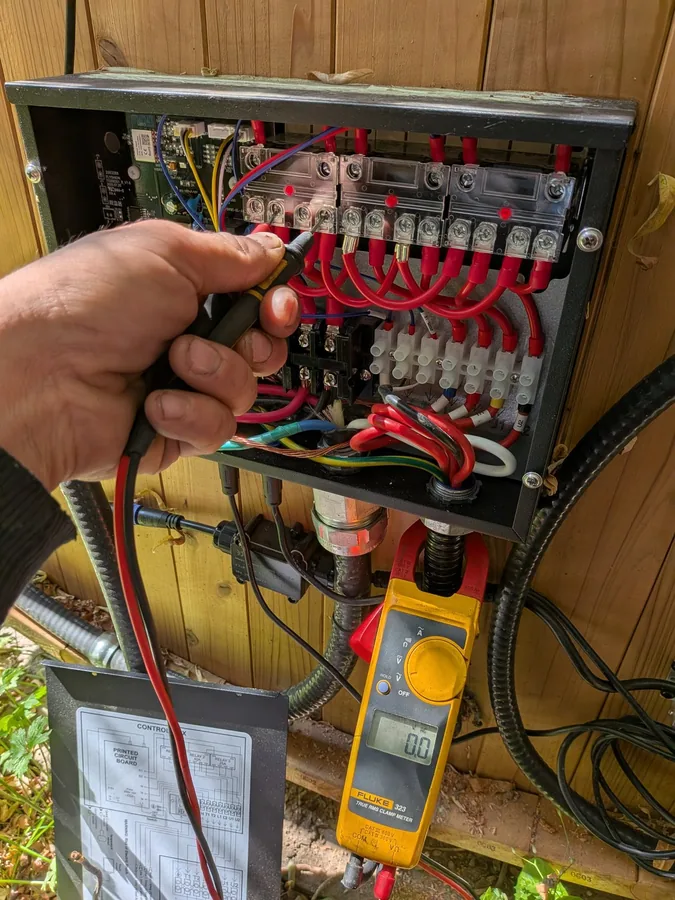 Electrician testing terminals inside a wired electrical enclosure with a clamp meter